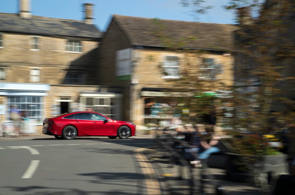 The real Toyota Mirai car passes the Cornish Bakery in Bourton-on-the-Water.
